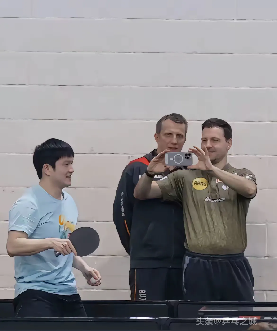 波尔开心的拿着手机给好友樊振东拍照,德国队教练罗斯科夫也高兴的合