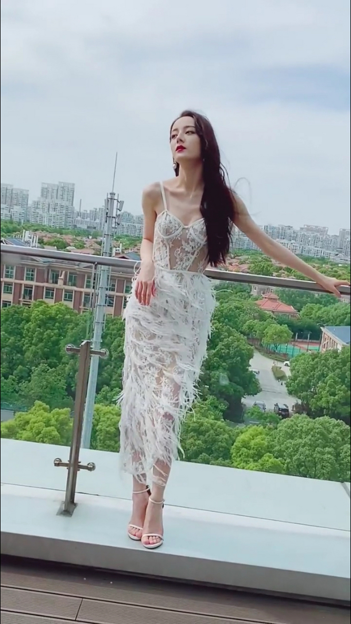 迪丽热巴,身着一套白色镂空蕾丝羽毛连衣裙,气质十分高雅,轻风吹拂之