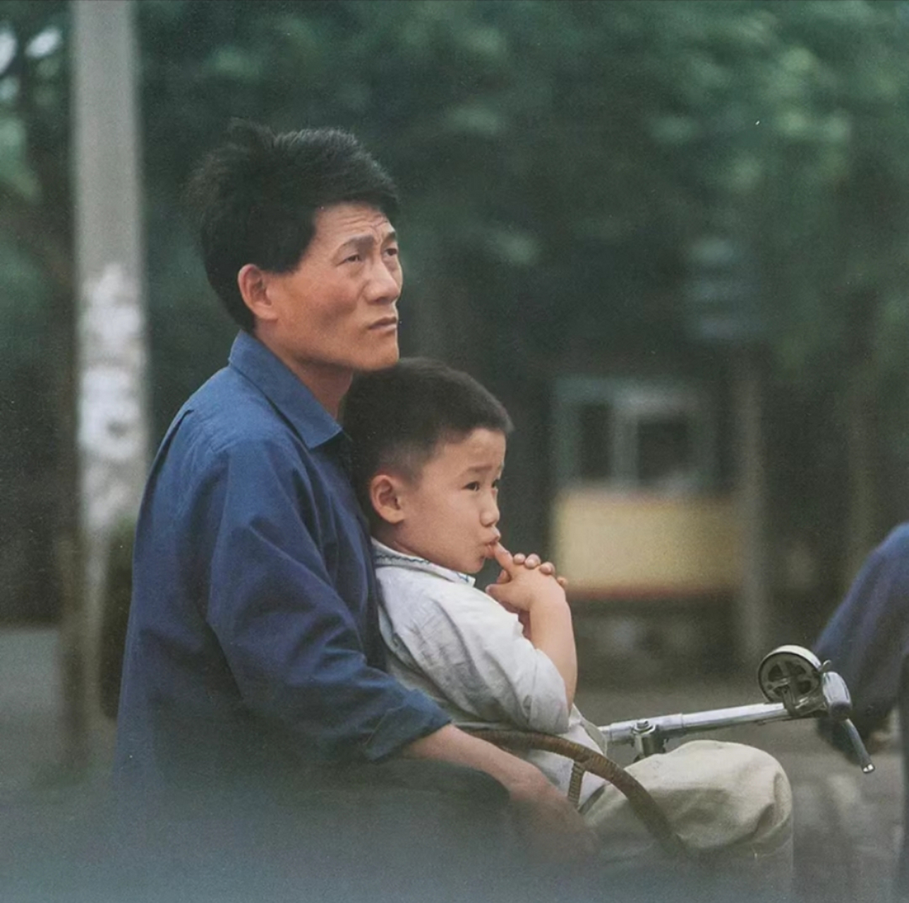 八十年代,上海老照片,父亲用自行车驮着儿子,正在向远处张望,父亲穿着