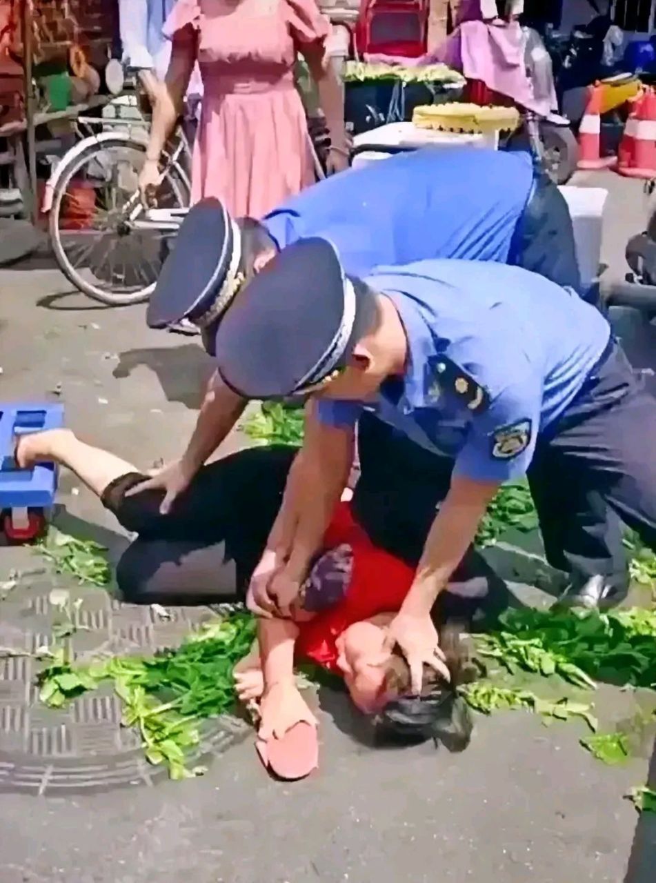 妇女手中紧握着拖鞋,但被城管按住动弹不得,地上散落着各色蔬菜.