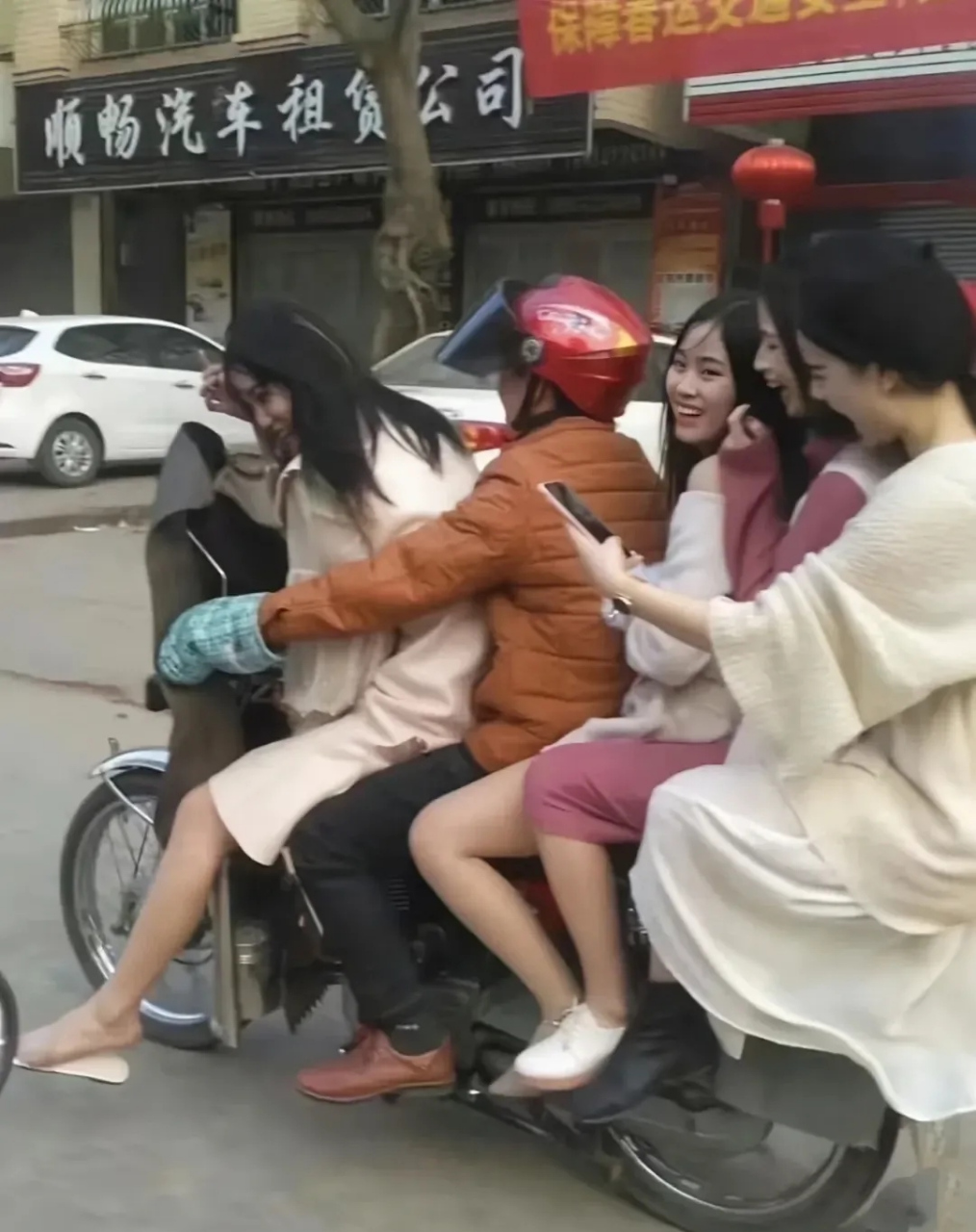 一女子骑摩托车超载,后面载两个人已经是挤挤的,坐最后面那个,还有