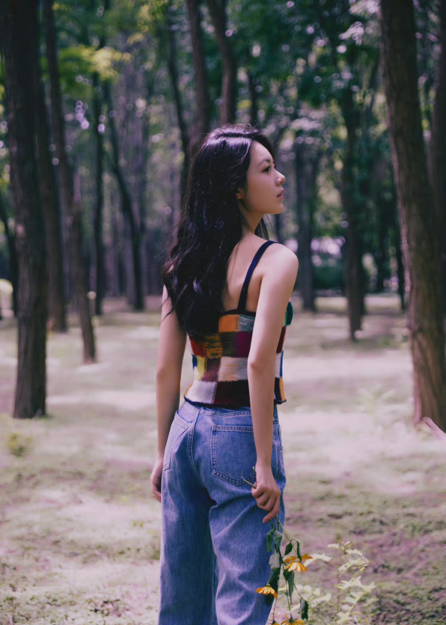赵今麦身穿多彩印花格纹针织吊带背心,搭配蓝色牛仔裤漫步于林间,灵动