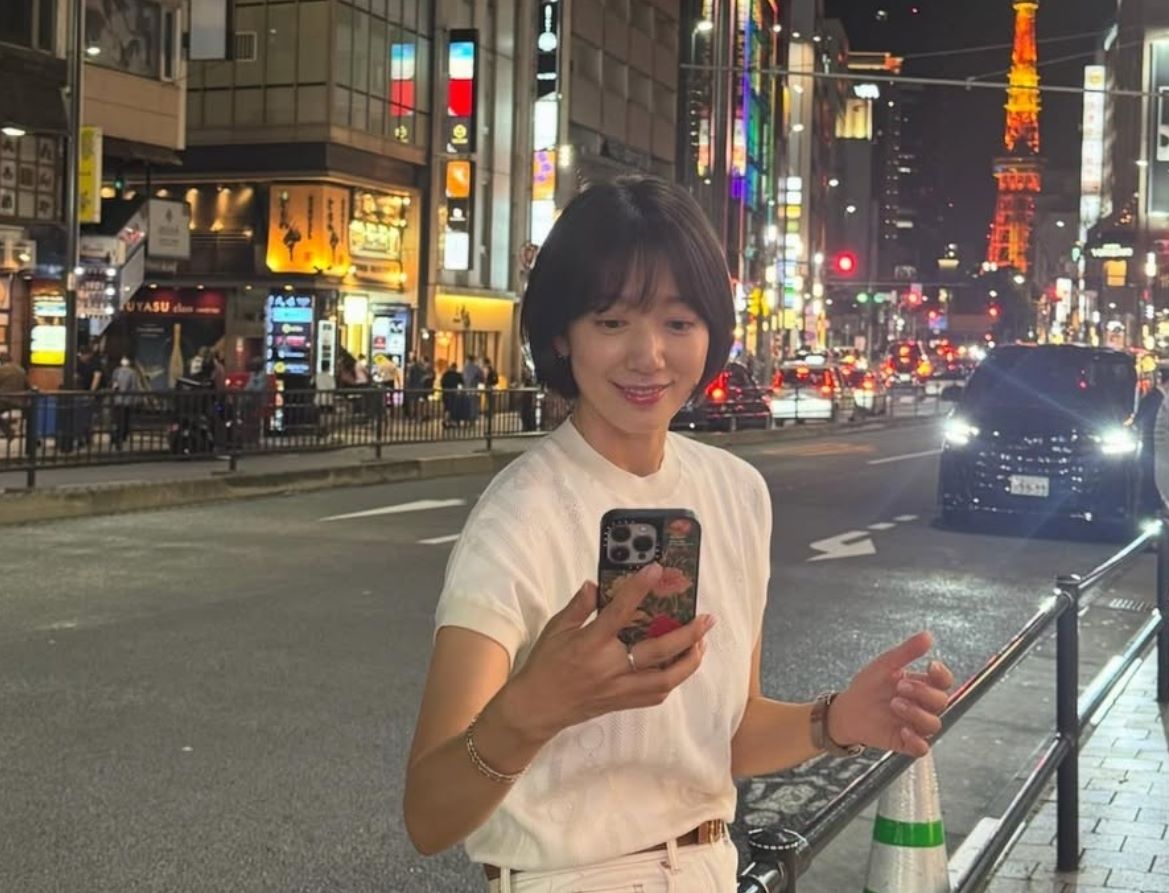 朴信惠身处日本东京塔下的街景中，一身全白的休闲装扮搭配短发