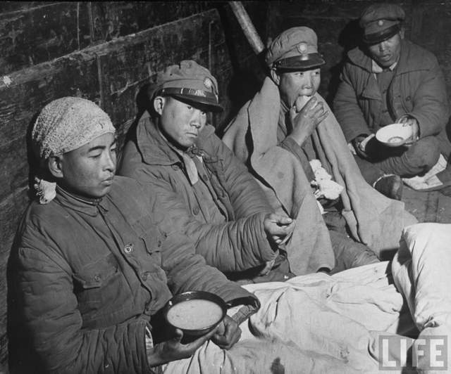 一座布满弹痕的岗楼内,几名伤兵身着血污破旧军装,坐在泥泞杂物间