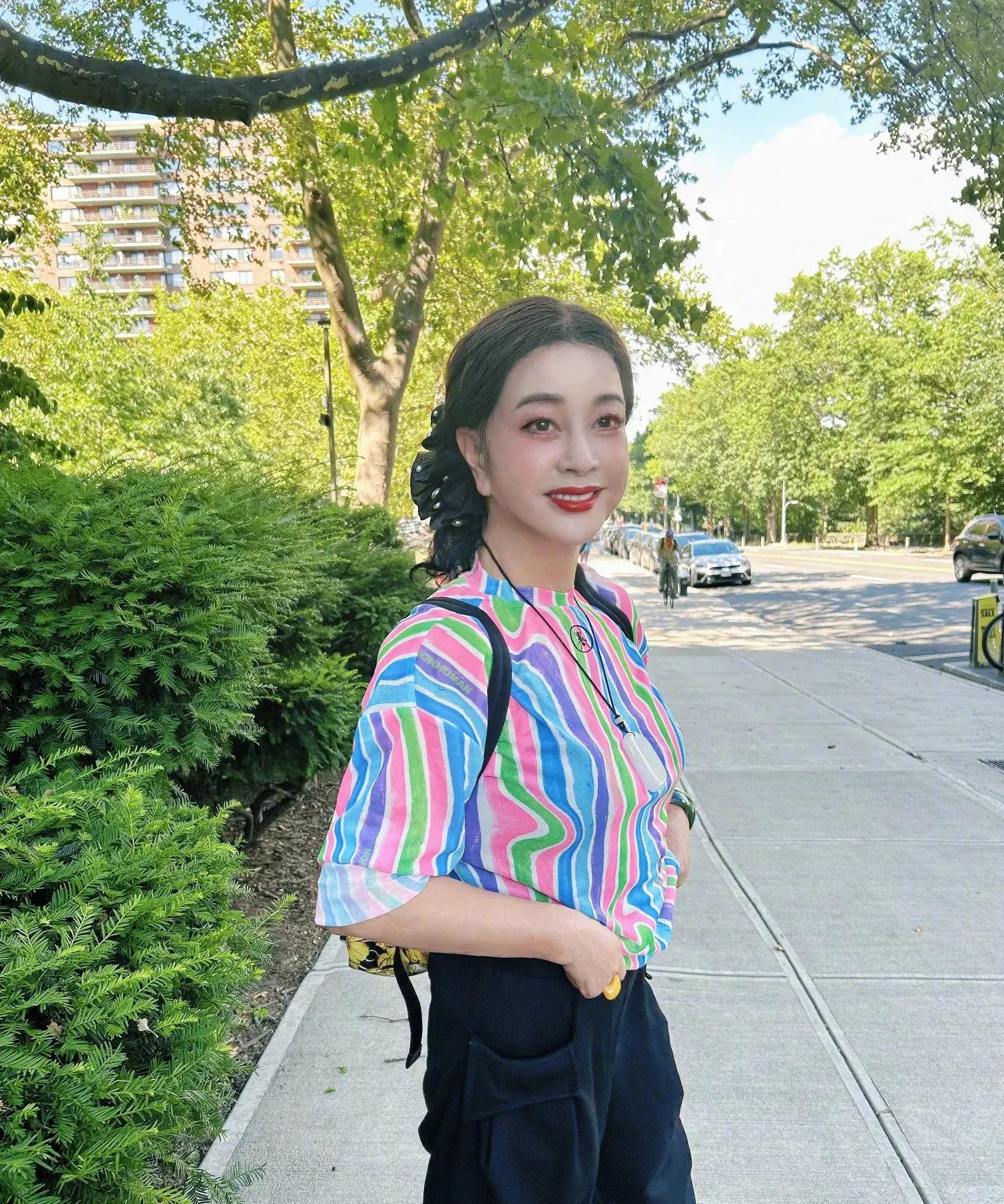 照片中刘晓庆身着明亮的彩虹色短袖,发型优雅地盘在脑后,妆容精致