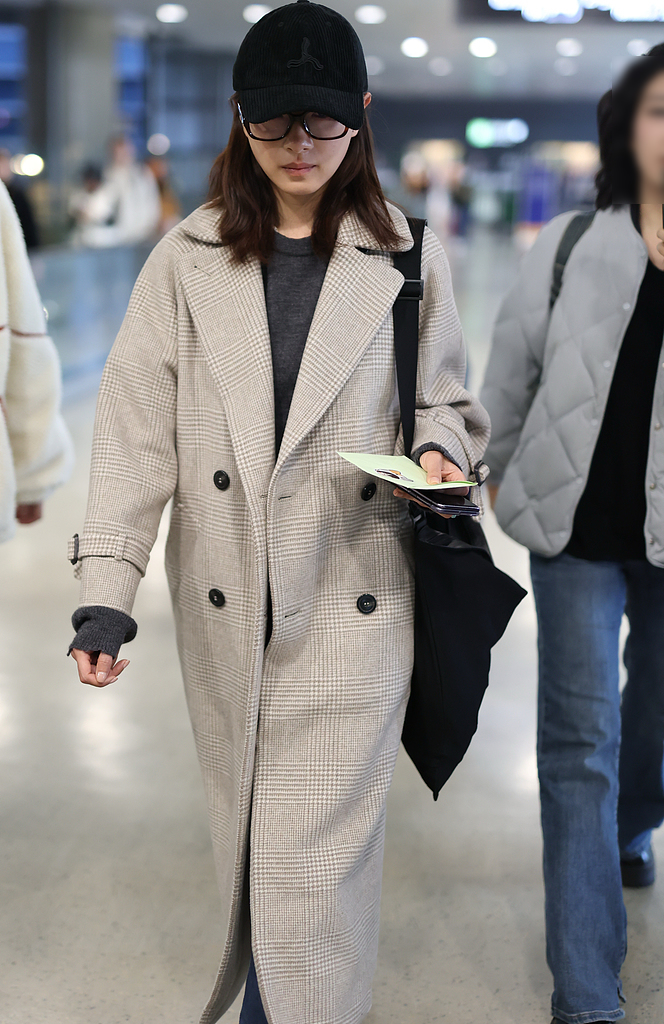 万茜机场街拍,她戴了一顶黑色的棒球帽,穿一件米色格子双排扣长款大衣
