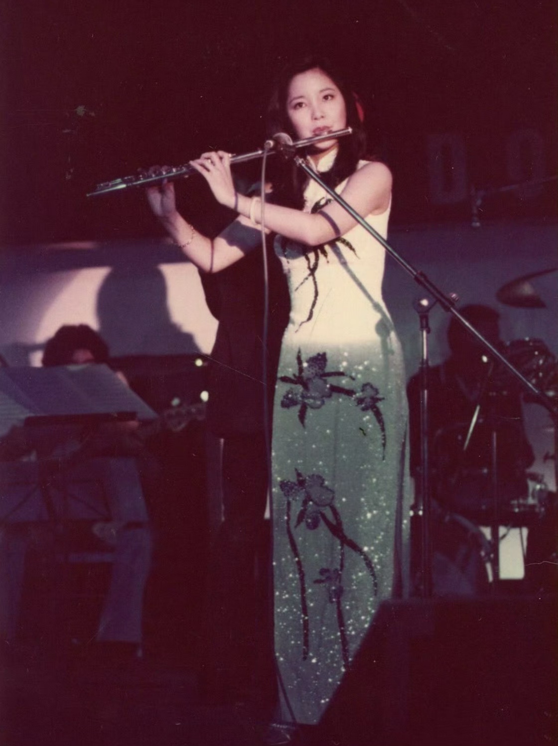 80年代,邓丽君在舞台上演出时的照片,她穿着精美的旗袍,吹着长笛,看着