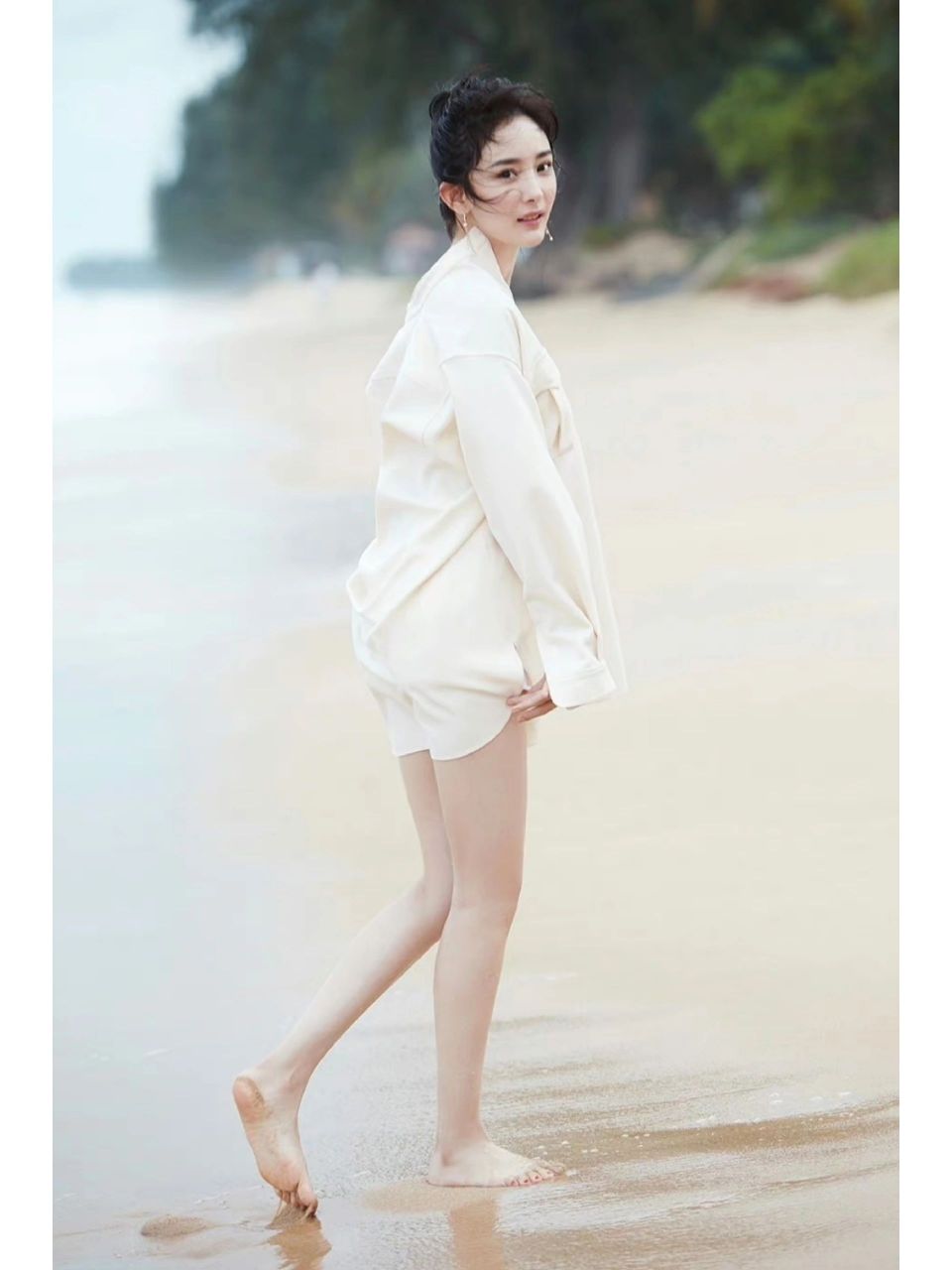 夏日份的杨幂,赤脚与海浪嬉戏|||穿着米白色小裙子 手拿鲜花 赤脚踩在