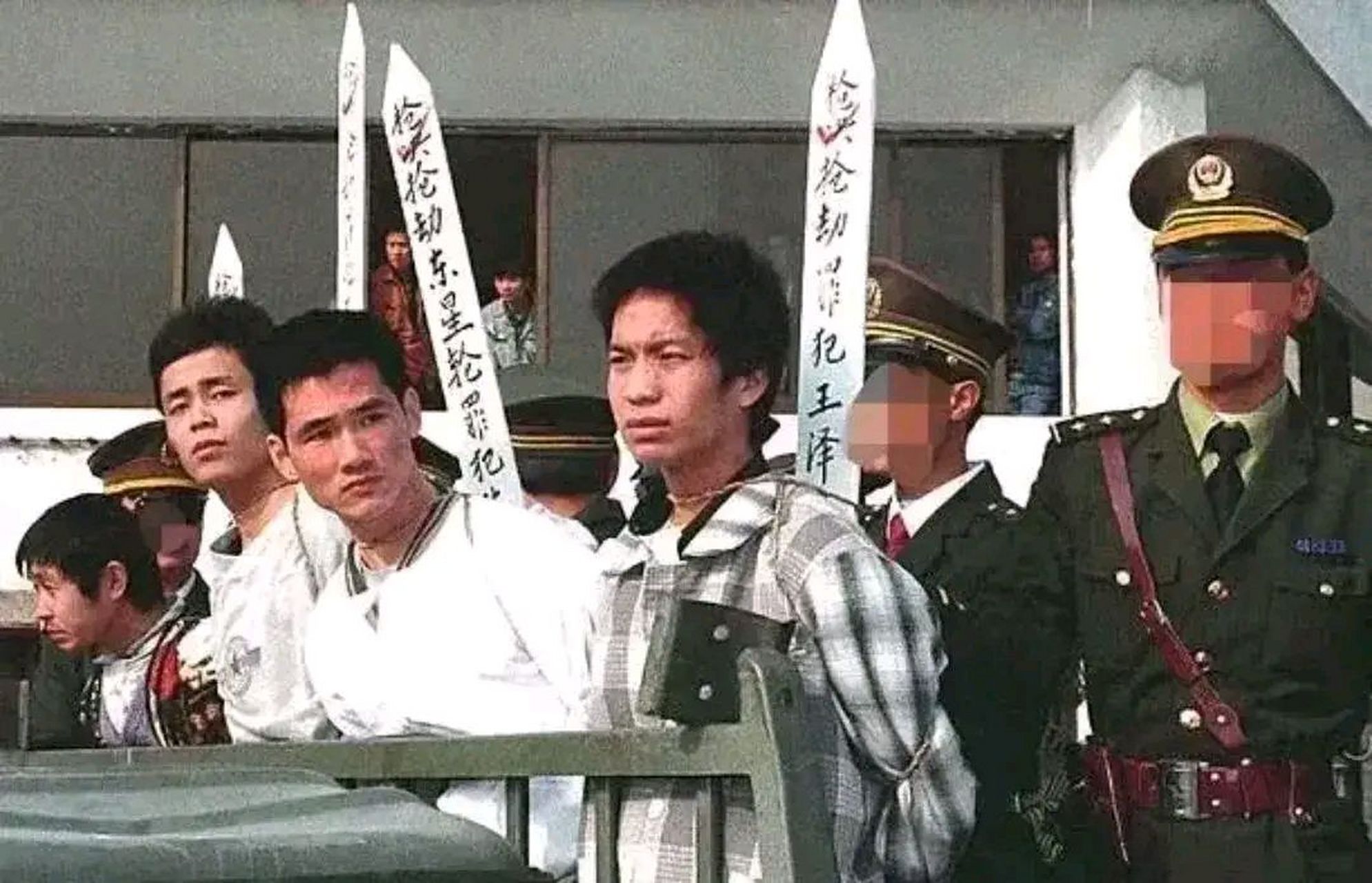 1996年,公审大会上,四名被五花大绑的死刑犯站在囚车上,后面站着高大