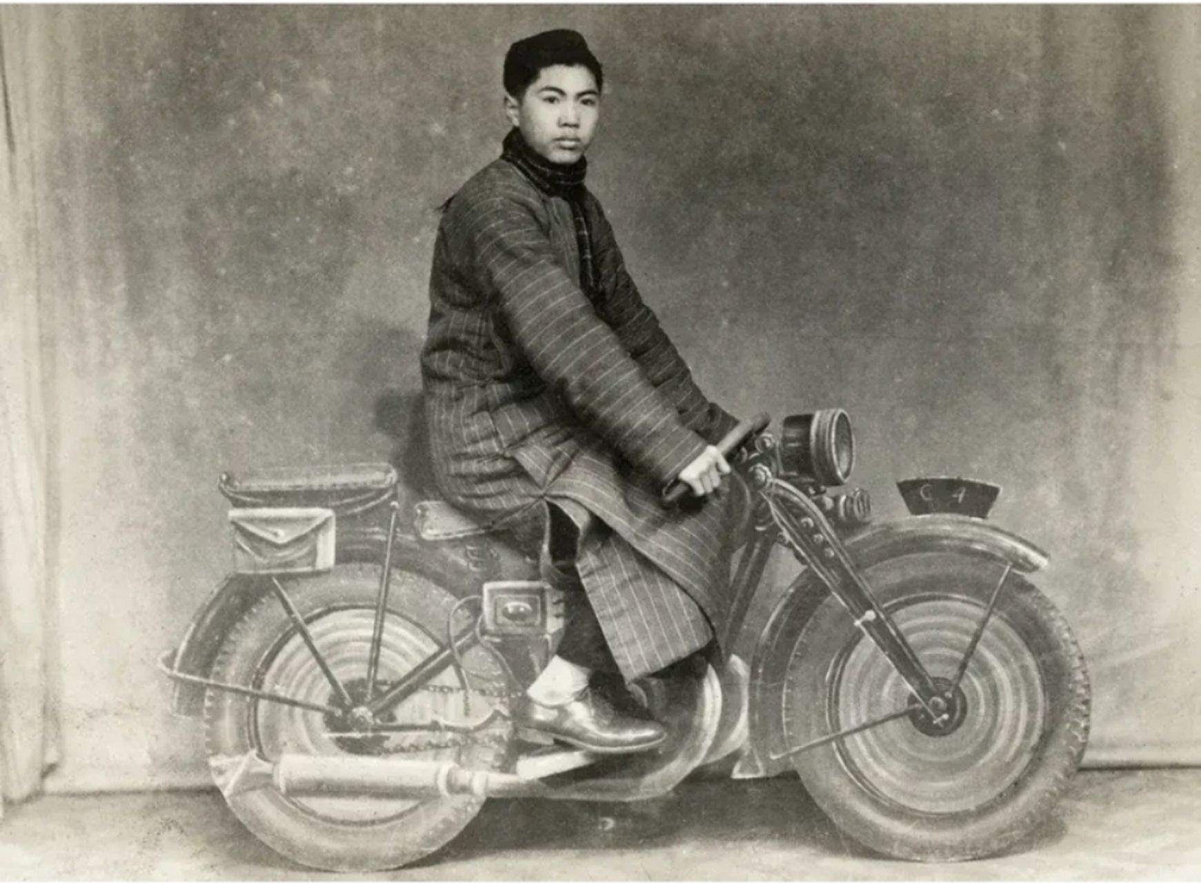 时期的老照片,照片中的年轻人身穿长衫,头戴围巾,骑着一辆大摩托车,他