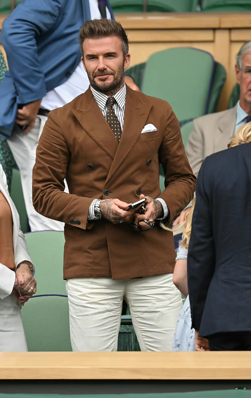贝克汉姆看球赛的穿搭造型,一身金棕色的西装搭配内搭白色条纹衬衫