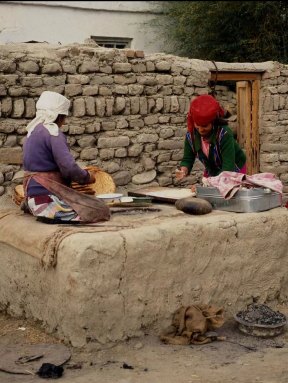 八十年代,新疆喀什地区,两位戴着头巾的少数民族女子,正在锅台上准备