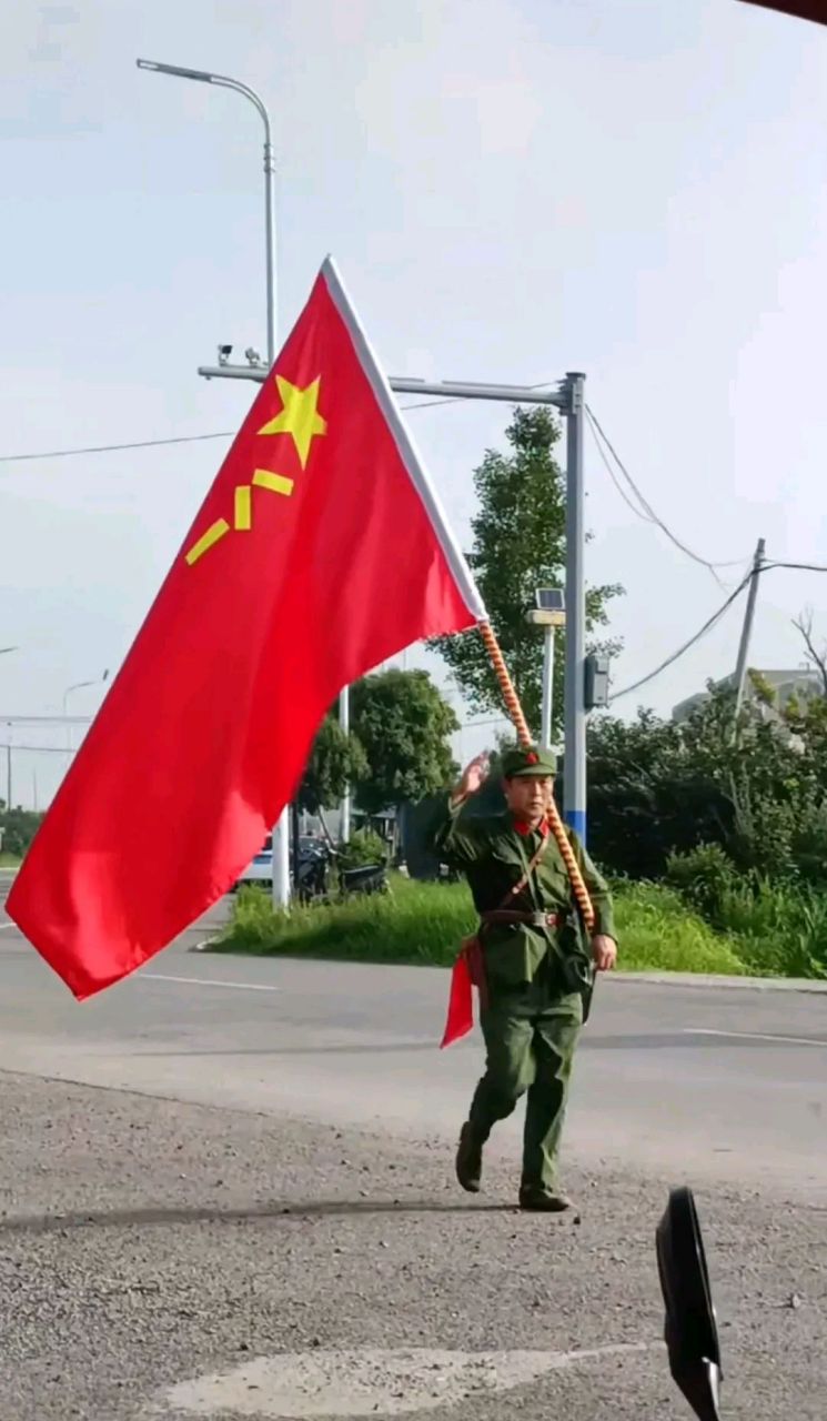 一位老兵肩扛八一军旗,步伐整齐地行走在大道上,从着装上看好像是一名