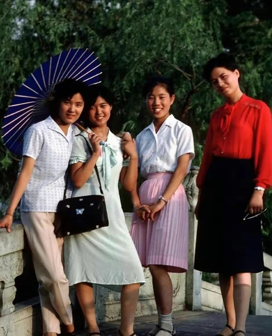 上世纪80年代上海的老照片,几个穿着时尚的少女撑着油纸伞在公园里面