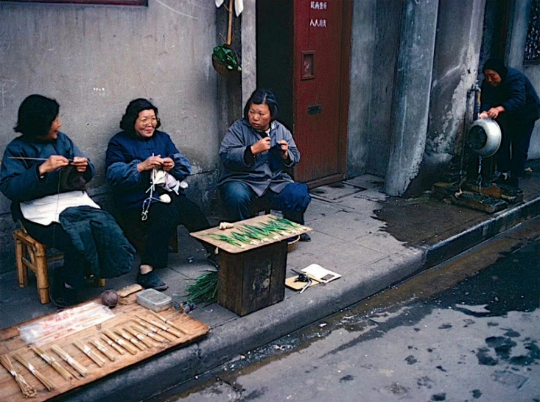 八十年代,上海某胡同,穿着朴素的家庭妇女坐在门前,边织毛衣边聊天,还