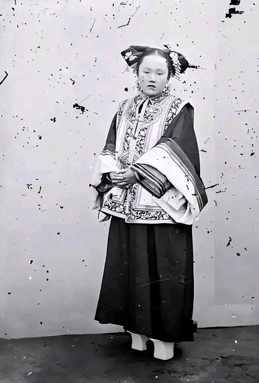 老照片:晚清时期,一个旗人女子,梳着精美的发式,身穿华丽的旗装,脚穿