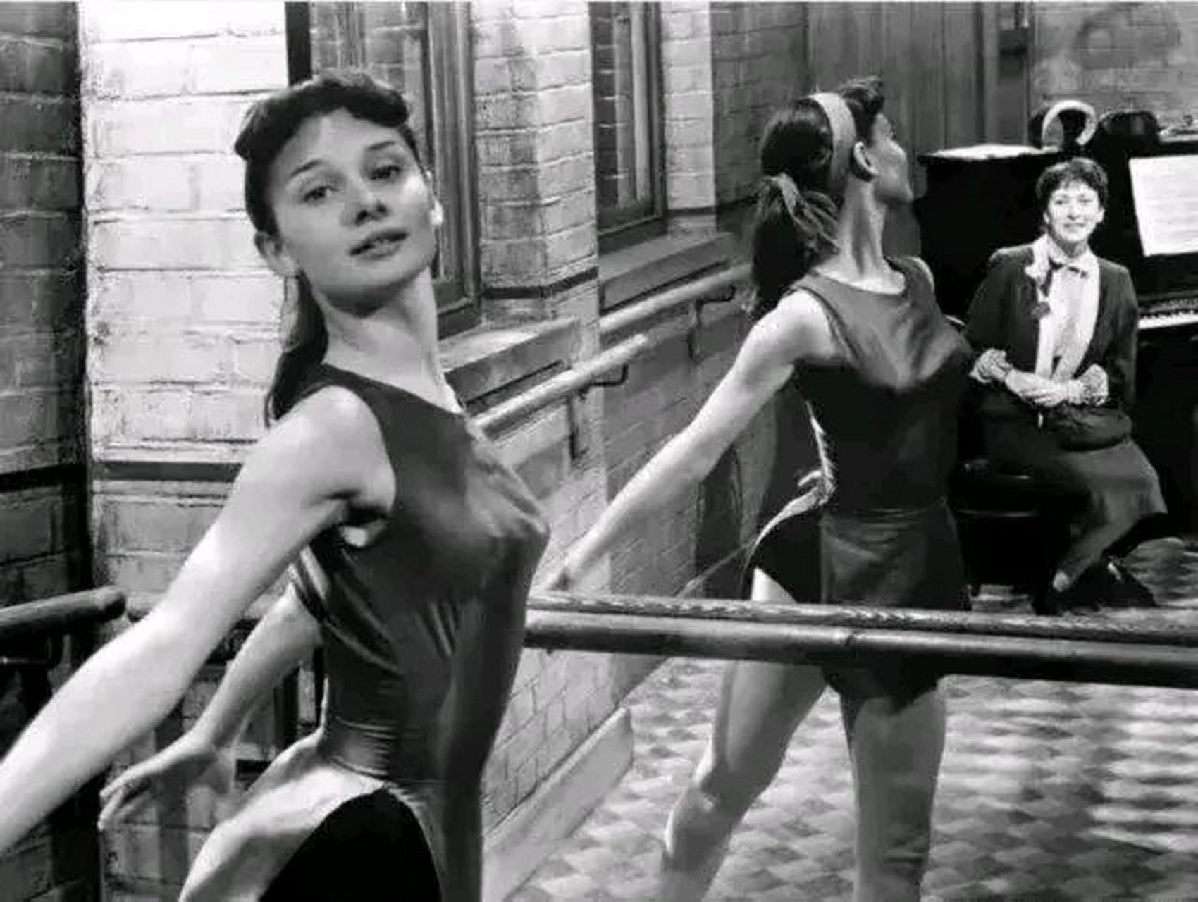 照片中赫本穿着一件紧身舞蹈服,扎着一个单马尾,正做着舞蹈动作,姿势