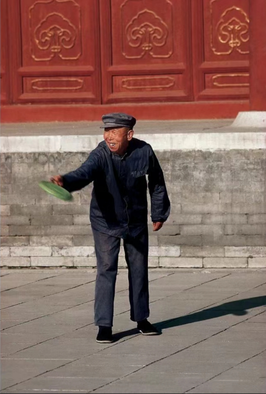 八十年代,北京街头,一位穿着朴素的老大爷,拿着疑似绿色的飞碟,后面是