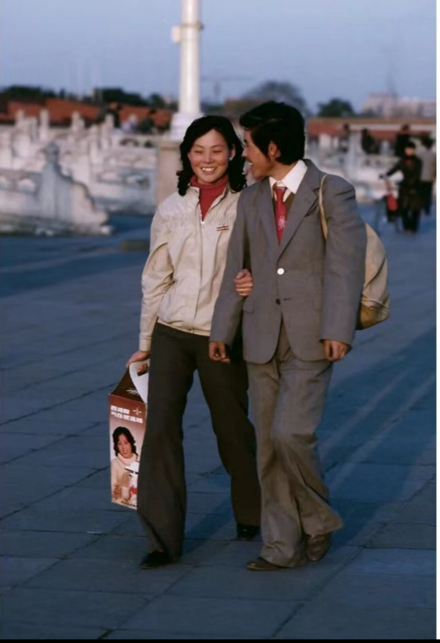 八十年代,北京天安门广场的一对情侣,男人穿着衣服,背着行李包,女人烫