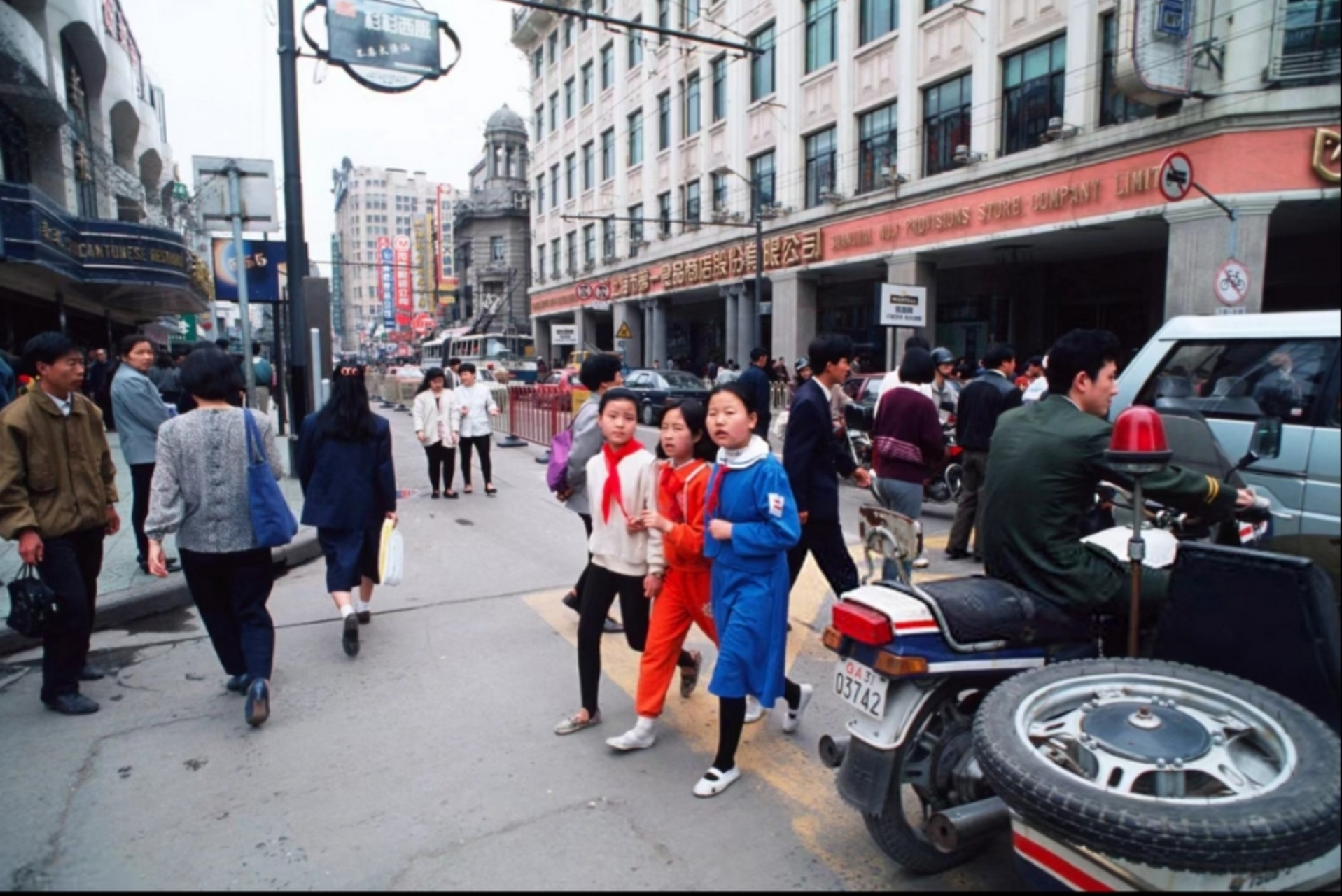 1995年,上海街头,三名戴着红领巾的女学生在过马路,旁边一位警察骑着