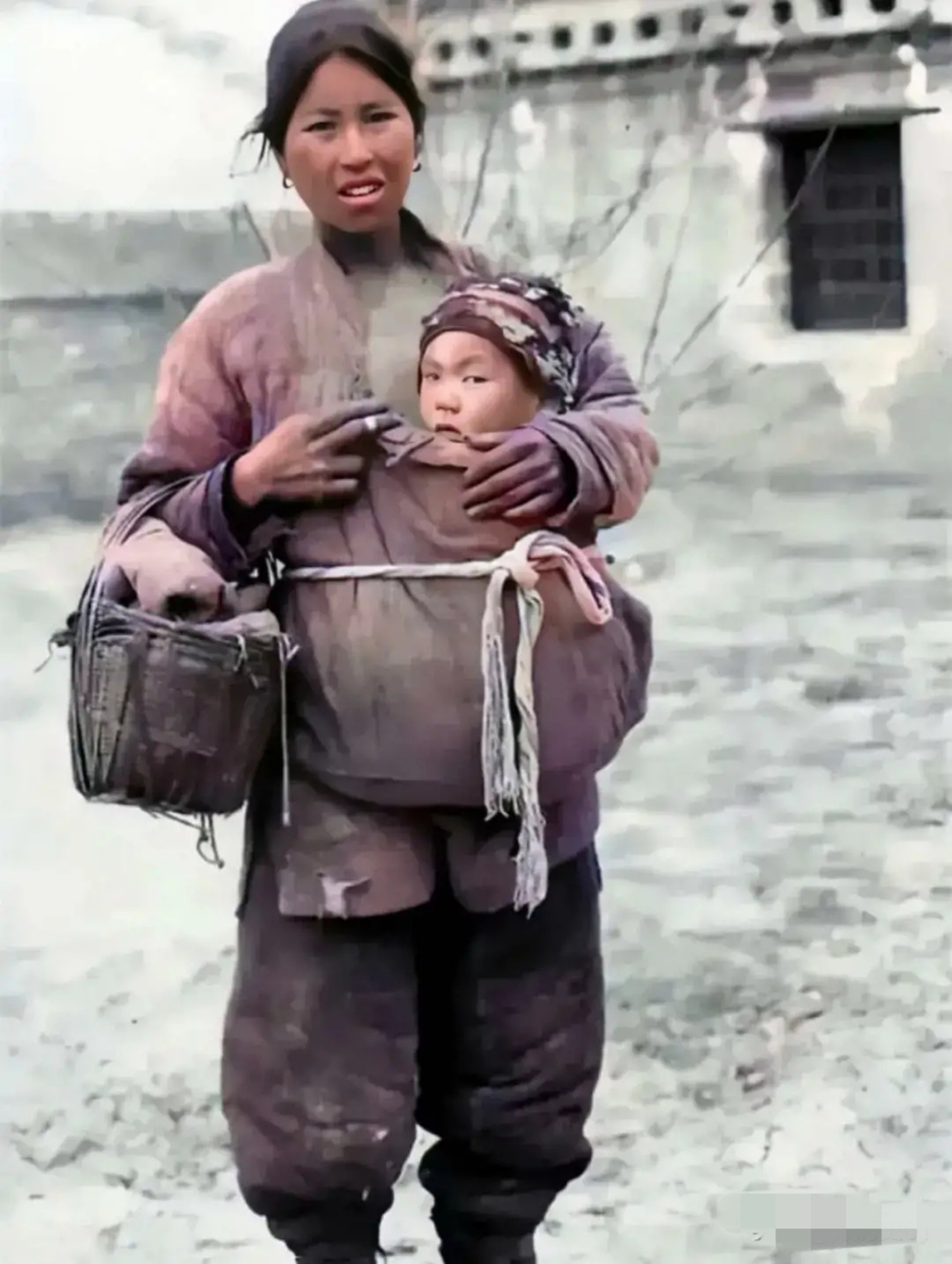 民国时期老照片:照片中,一个挎着篮子的女人怀抱着自己的孩子,在冰天