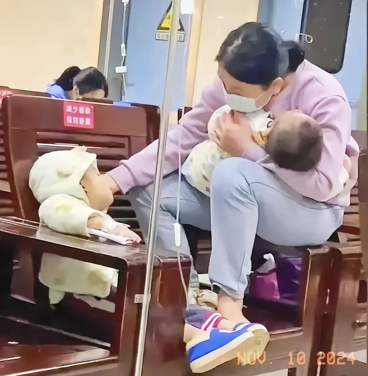 网友心酸了:医院的椅子上,一位妈妈坐在椅子的扶手上,怀里抱着一个
