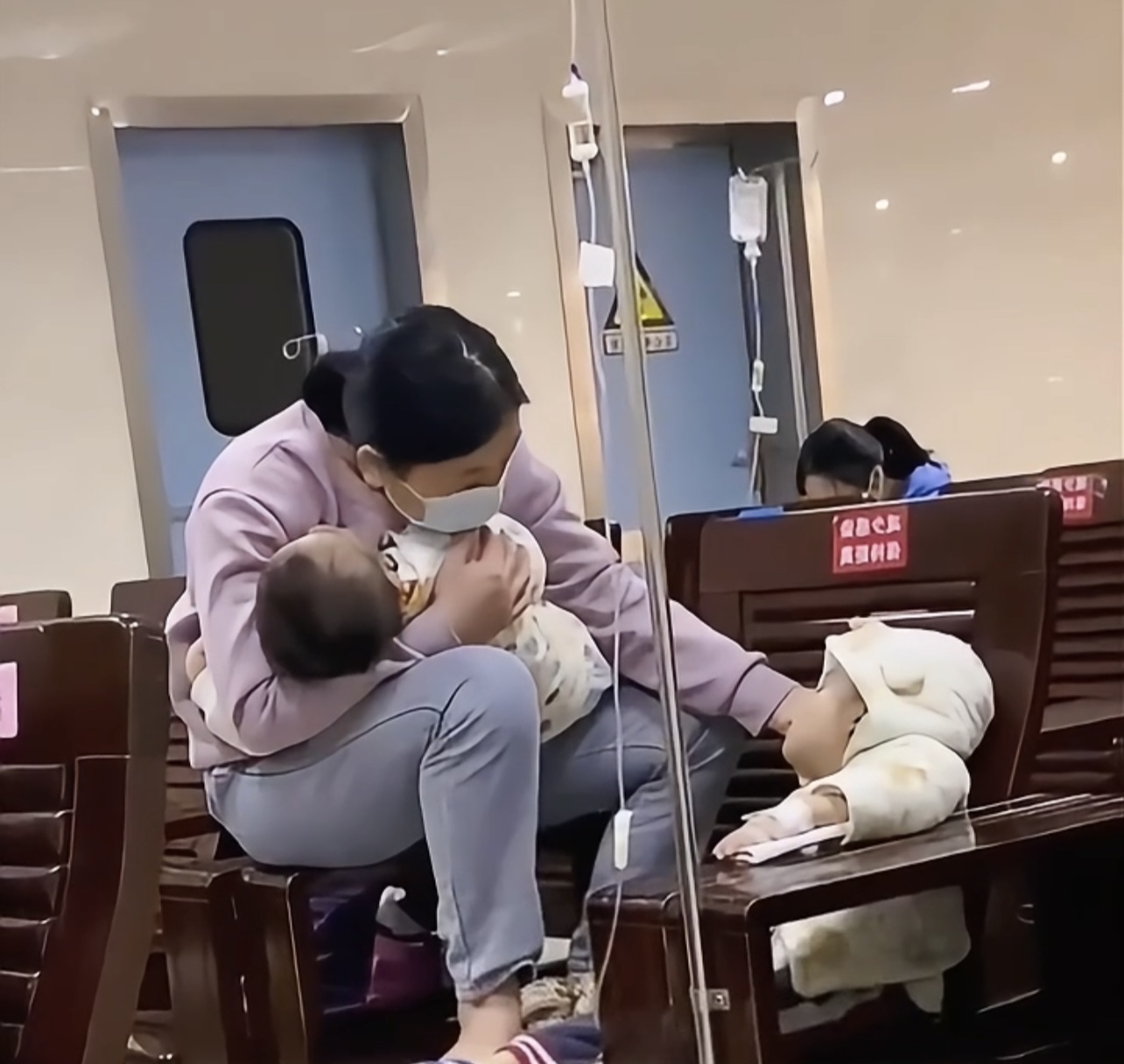 着两个孩子,大宝生病了在输液,小宝已经酣然入睡,妈妈一手抱着睡梦中