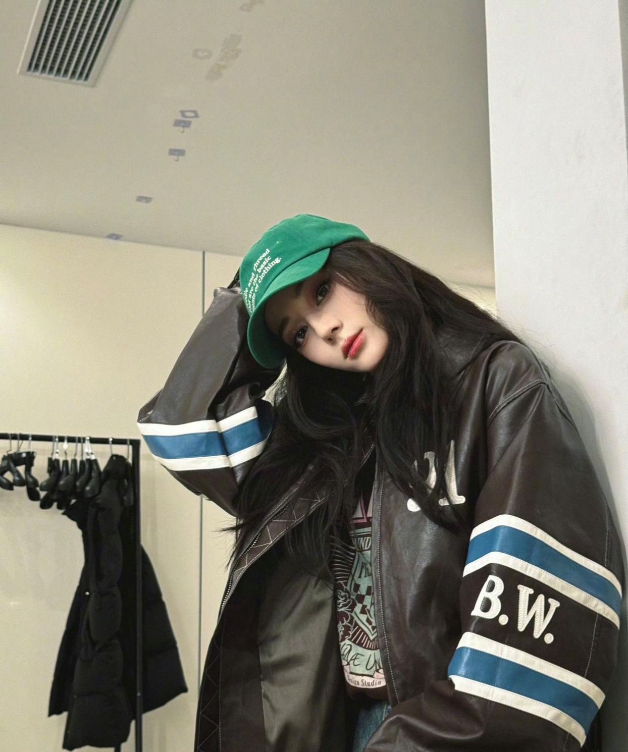 服风格的皮质夹克外套,搭配了蓝色牛仔裤和白色板鞋,头戴绿色棒球帽