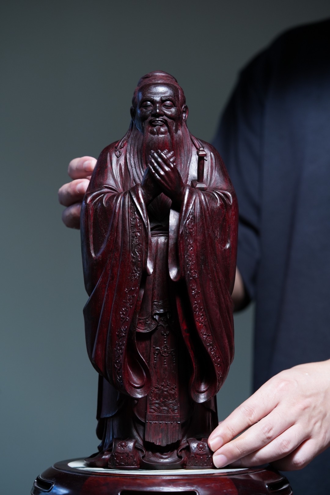 孔子束发髻,着儒服,眉目生动传神,稳重慈祥,双手交叠行礼,气宇谦和