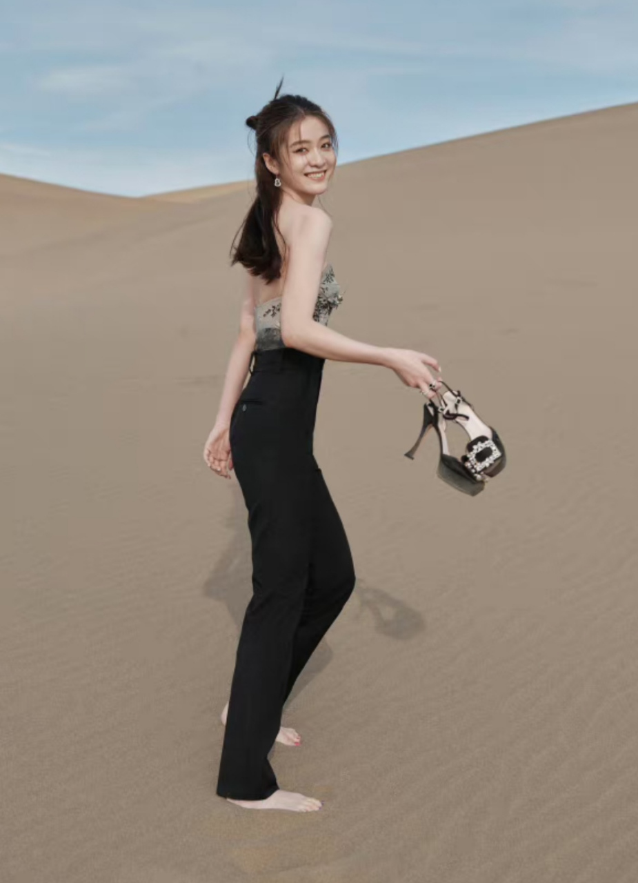 张雪迎在沙漠里参加活动,高跟鞋站不稳,用手提着拍照,回身看镜头甜笑
