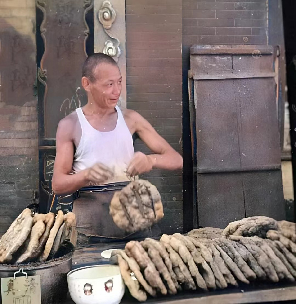 1941年,北平一名穿着背心的男子正将出锅的大油饼摆在案板上,在案板上