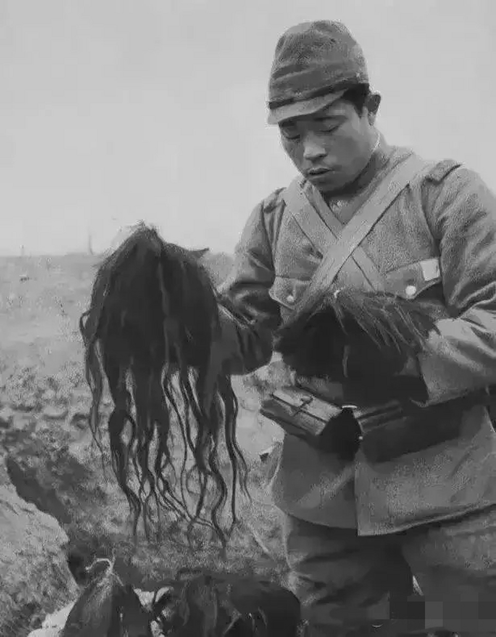 抗日战争时期,一个日寇正在欣赏刚刚从中国人头上剥下来的头发,旁边还