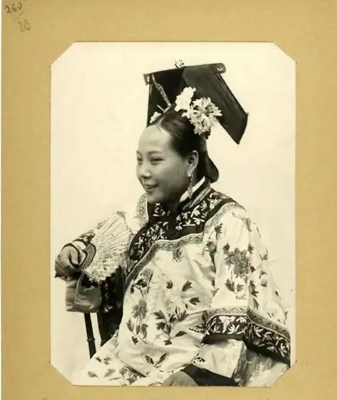 外国公使拍摄的满族美女照片,她身穿华丽的传统服饰,头戴大拉翅,手拿