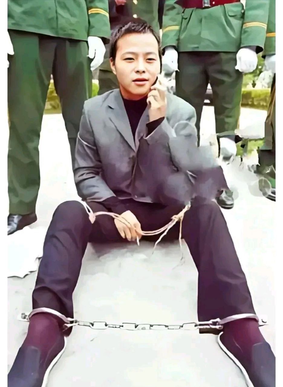 照片中的死刑犯身上绑着法绳,脚上戴着铁链,右手夹着香烟,左手拿着