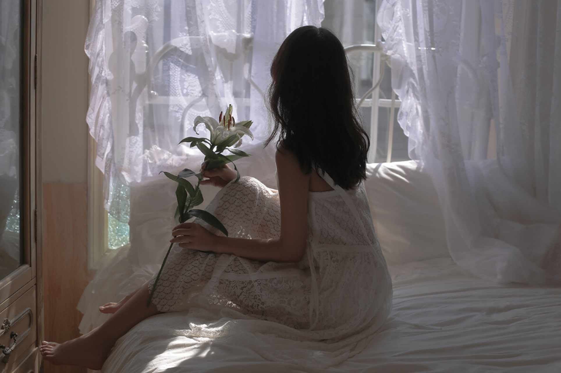 在慵懒的午后,一位身着白色蕾丝吊带裙的长发美女静静躺在床上,为房间