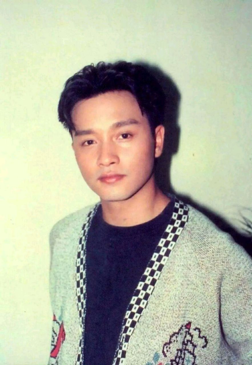 年少的张国荣站在家门口前,身穿一件碎花衬衫,下穿一条灰色的西裤