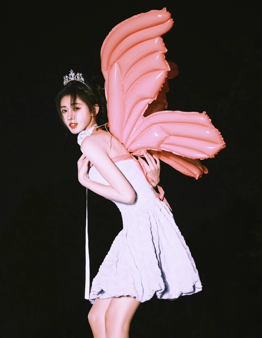 照片中,鞠婧祎穿着粉紫色连衣裙, 头戴皇冠,背着粉色充气翅膀, 身材