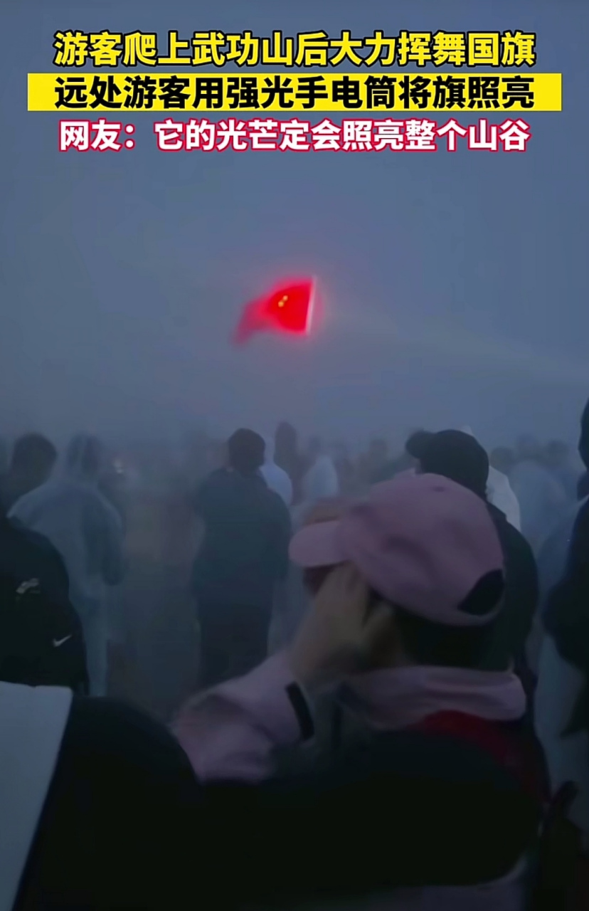 游客爬上武功山后大力挥舞国旗,远处游客用强光手电筒将旗帜照亮
