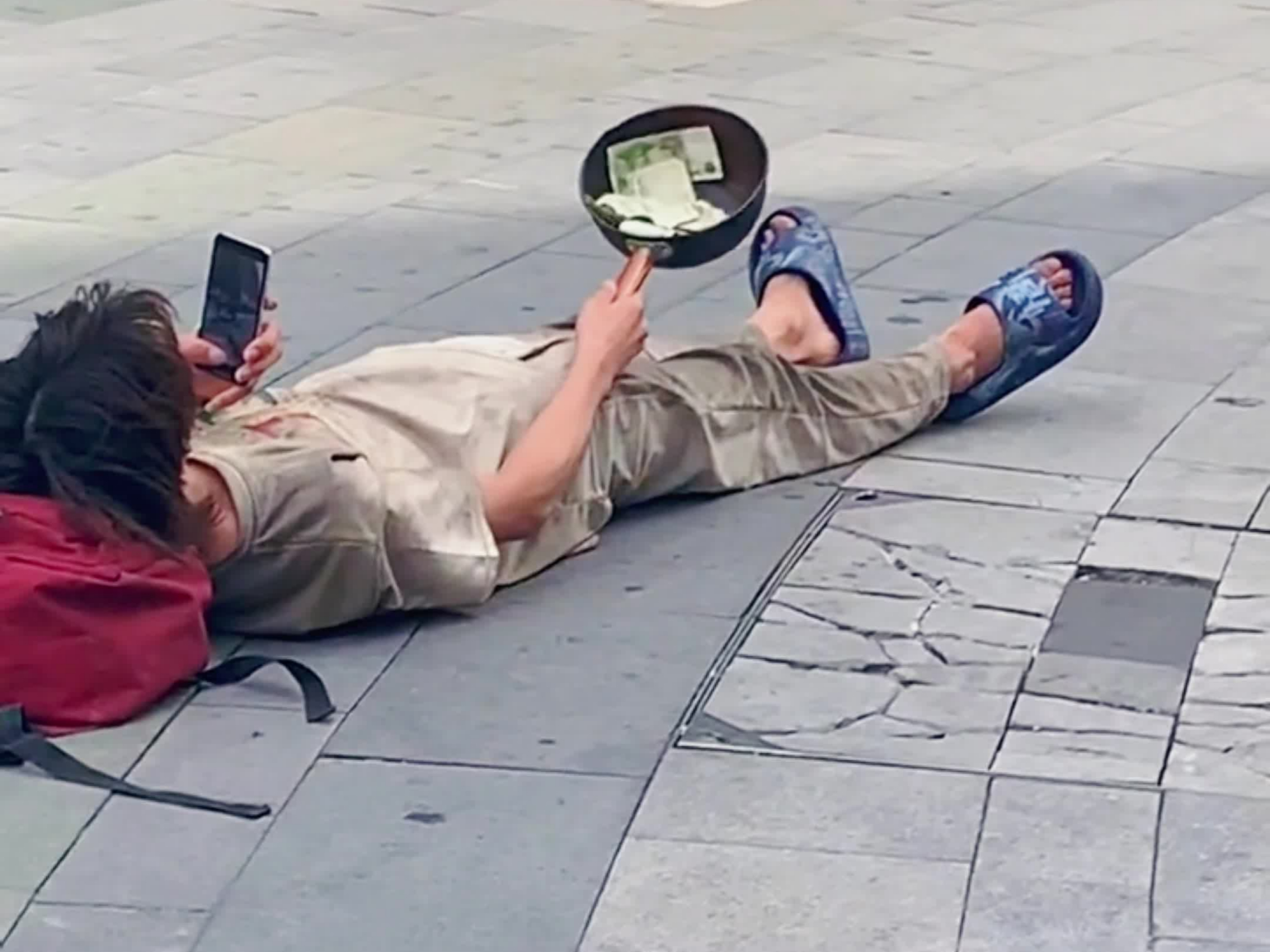 乞丐躺在路中间,一手端着盆要钱,一手玩手机,网友:"认真工作"的男人