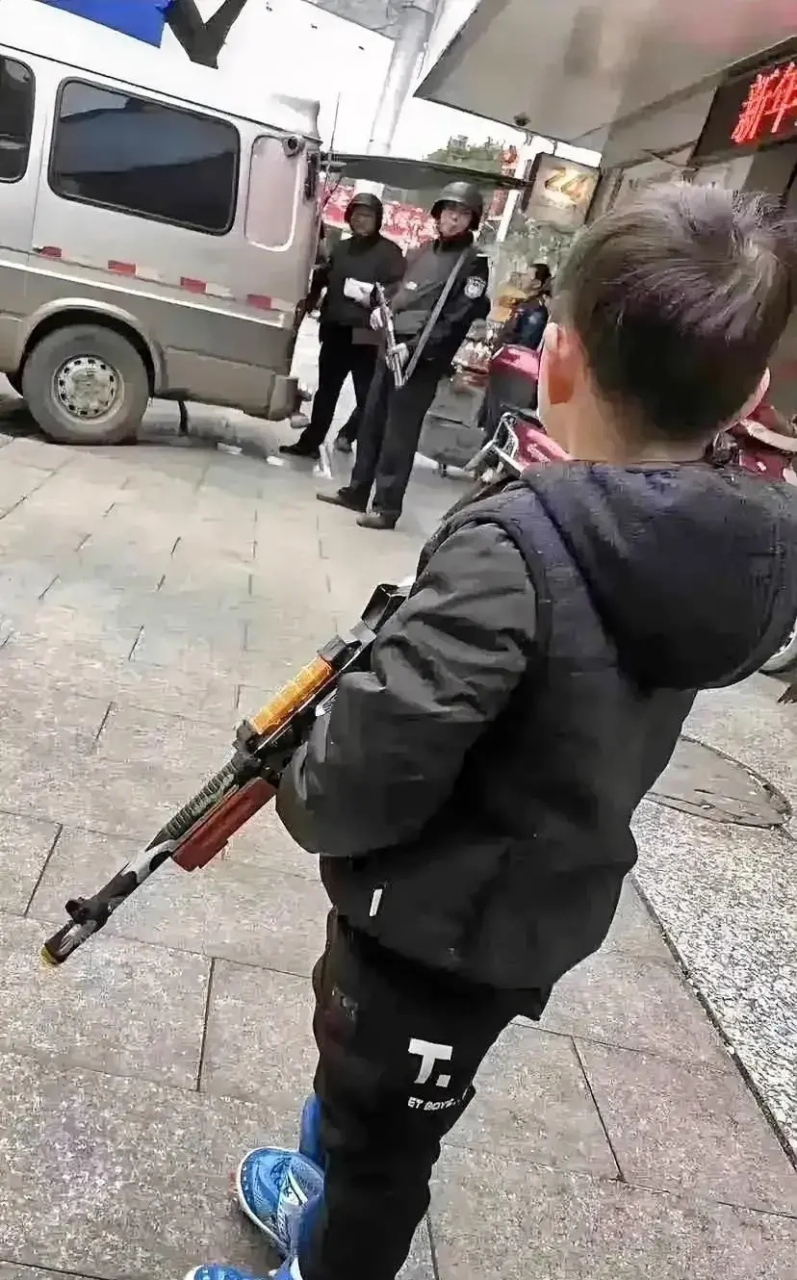 这个年幼的小男孩,拿把玩具枪站在了押运员的对面,看着持枪的押运员的