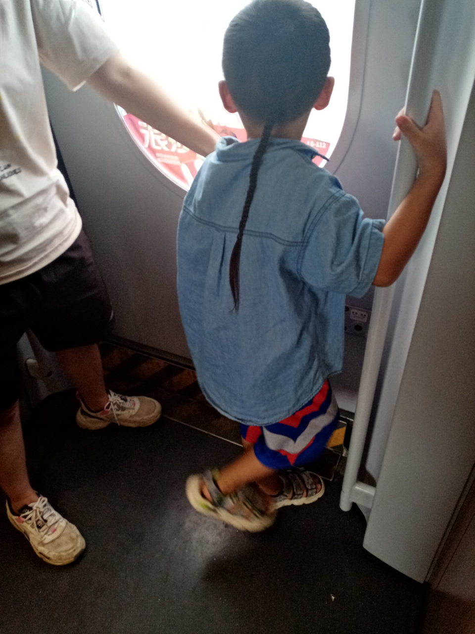 近日,我在高铁列车上看到一个留着小辫子的男孩,在车门处无忧无虑地