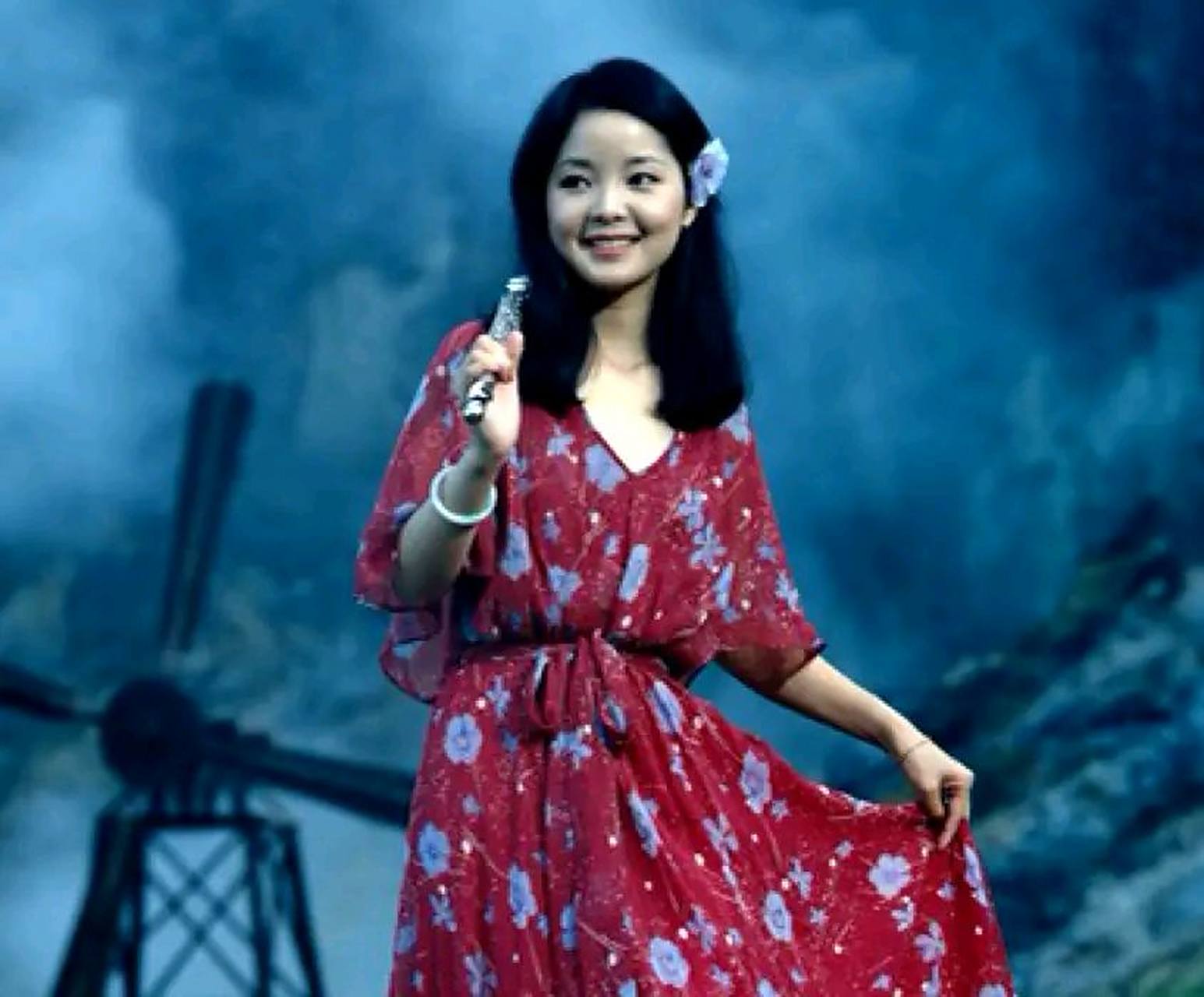 年轻时候的邓丽君在舞台表演时的留影,照片中邓丽君穿着一袭红衣,头上