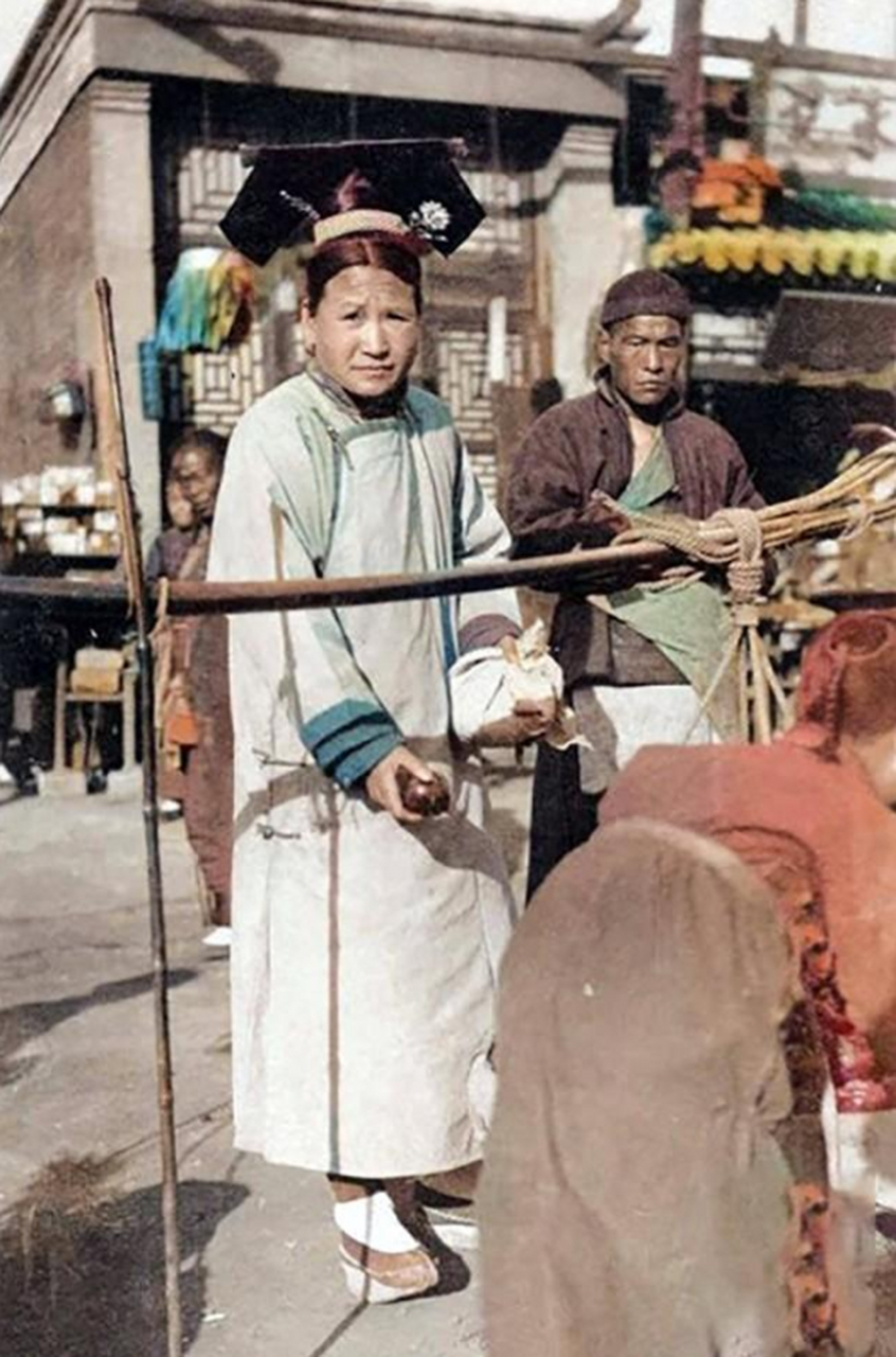 清末彩色老照片:一位正在逛集市买东西的满族妇女,她身穿满族的传统