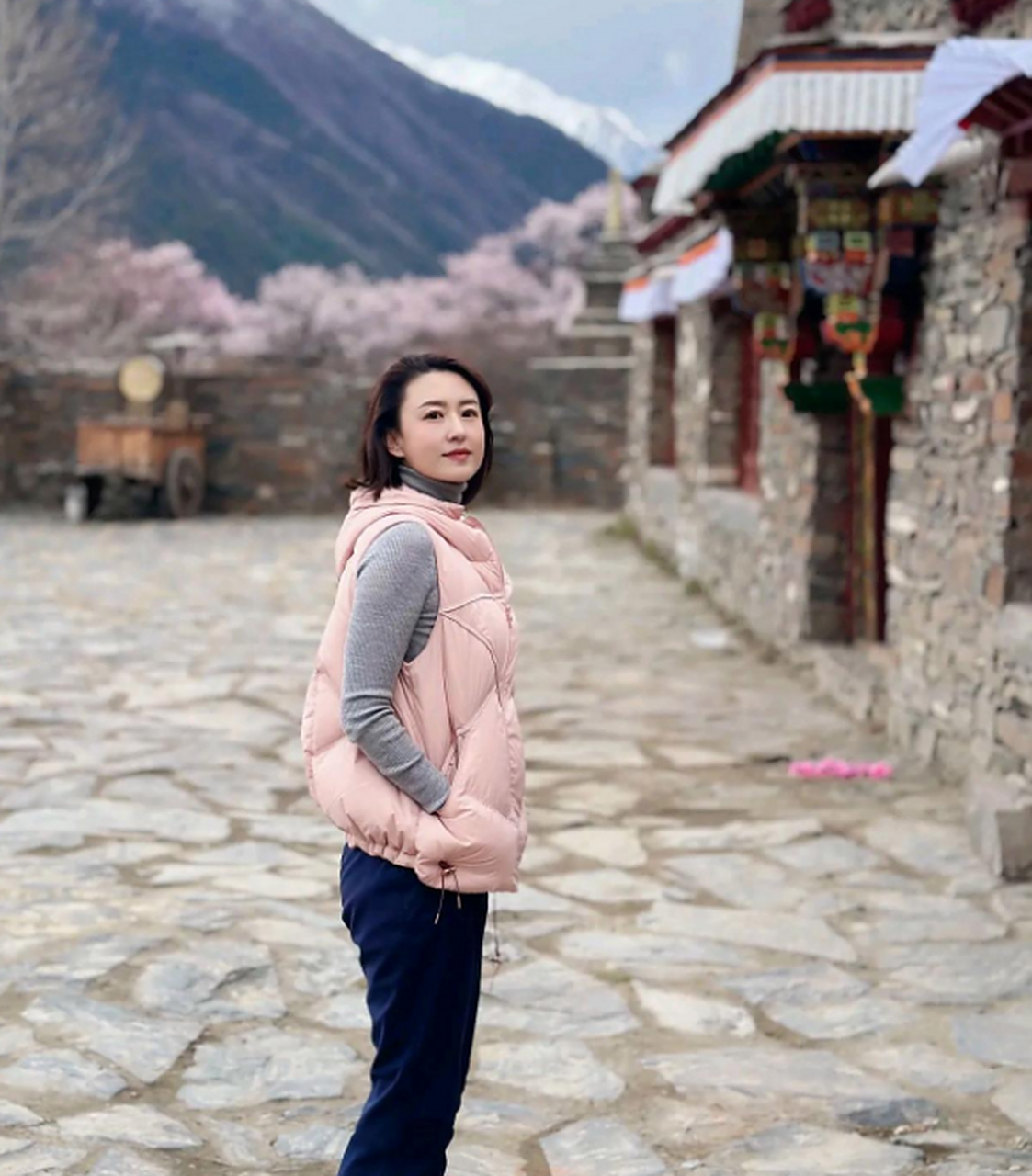 张蕾穿灰色高领针织衫,外搭粉色羽绒马甲,搭蓝色牛仔裤,五官端庄精致