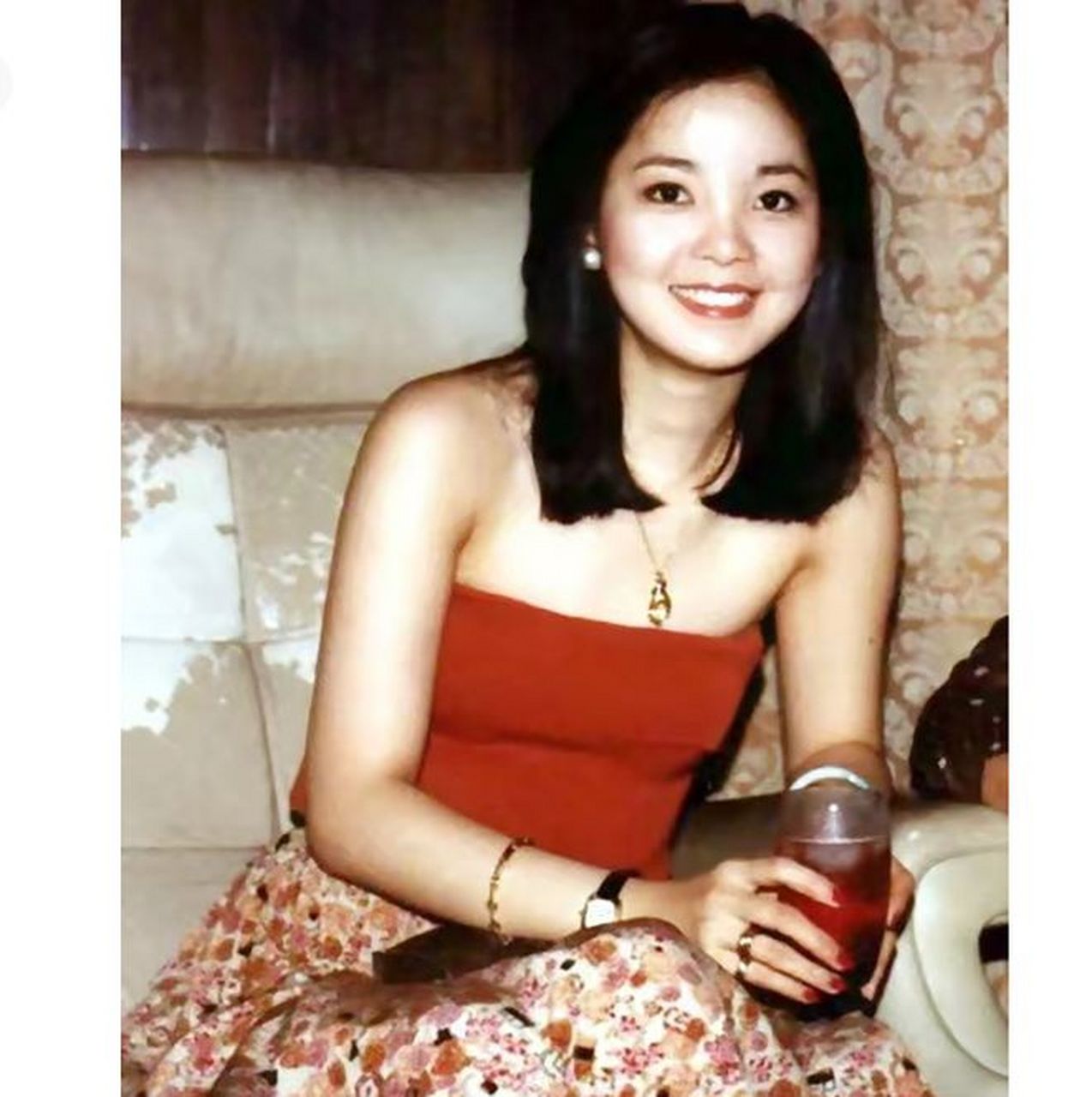 在一张年轻时的照片中,邓丽君穿着一件火红的抹胸上衣,搭配一条碎花