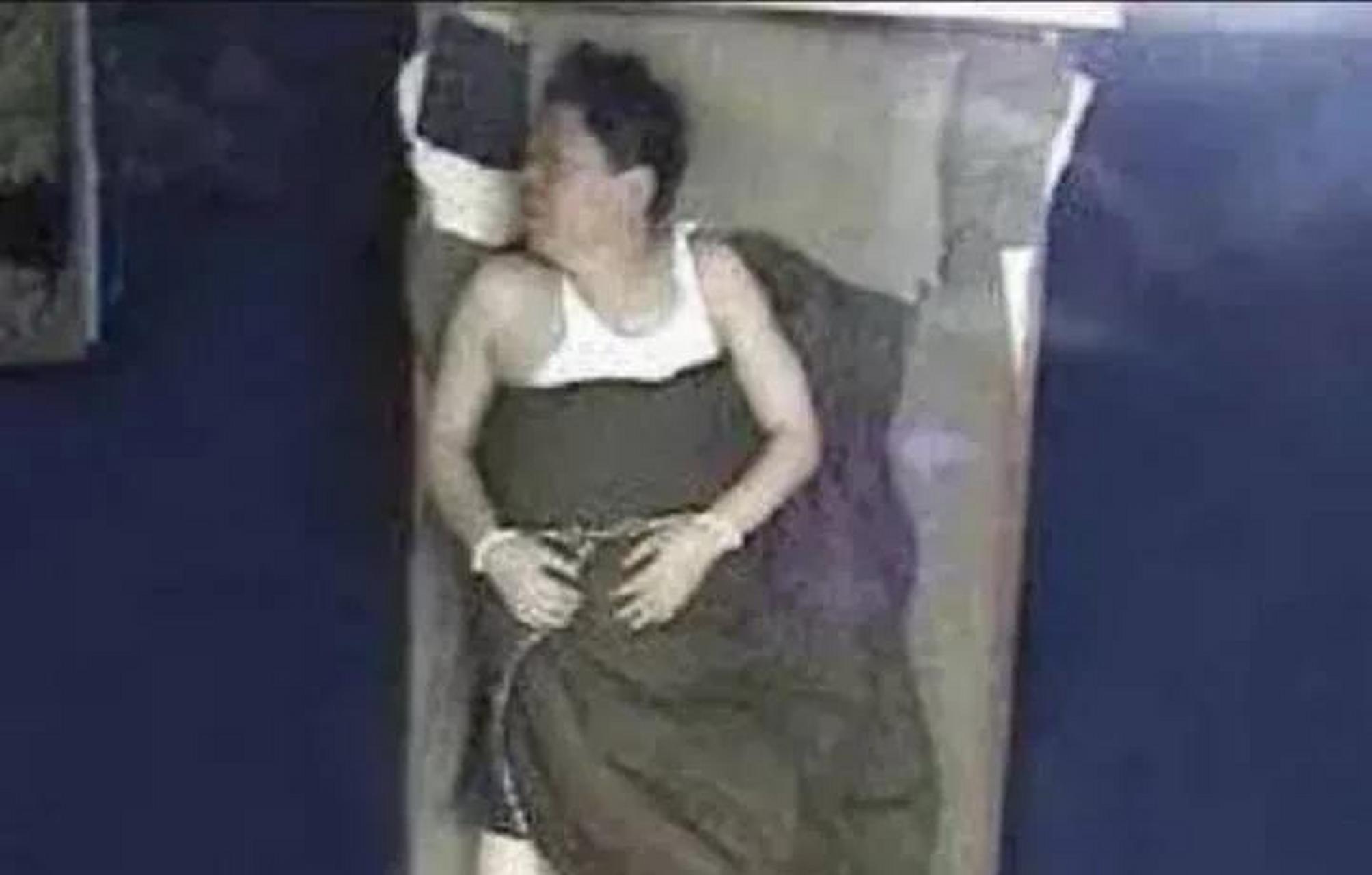 照片中的他穿着白色背心,戴着手铐,正躺在床上睡觉