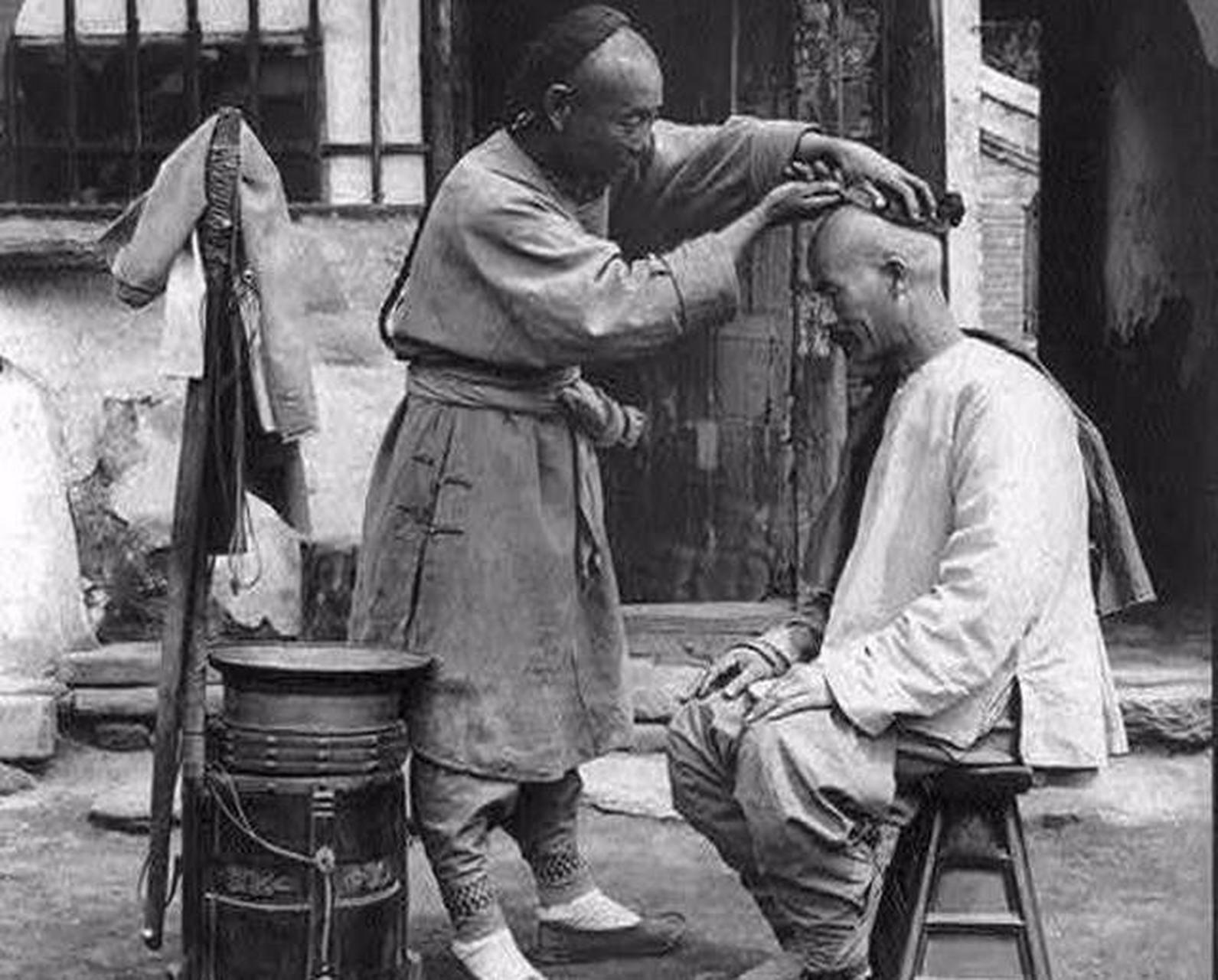 晚清时期,一名理发师娴熟的给客人剃发.