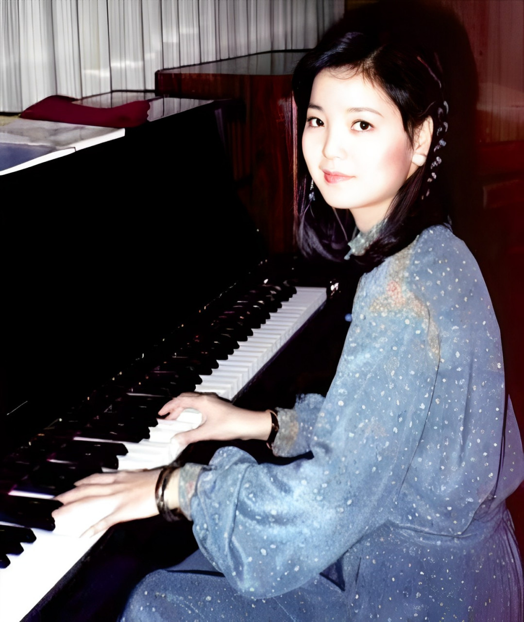 这是正在弹奏钢琴的邓丽君,照片中邓丽君身穿一身水蓝色斑点长裙,头上