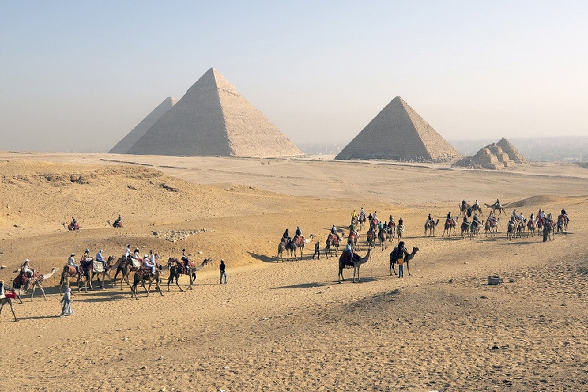 埃及提高旅游业投资 游客们骑着骆驼参观吉萨金字塔群景区,埃及.