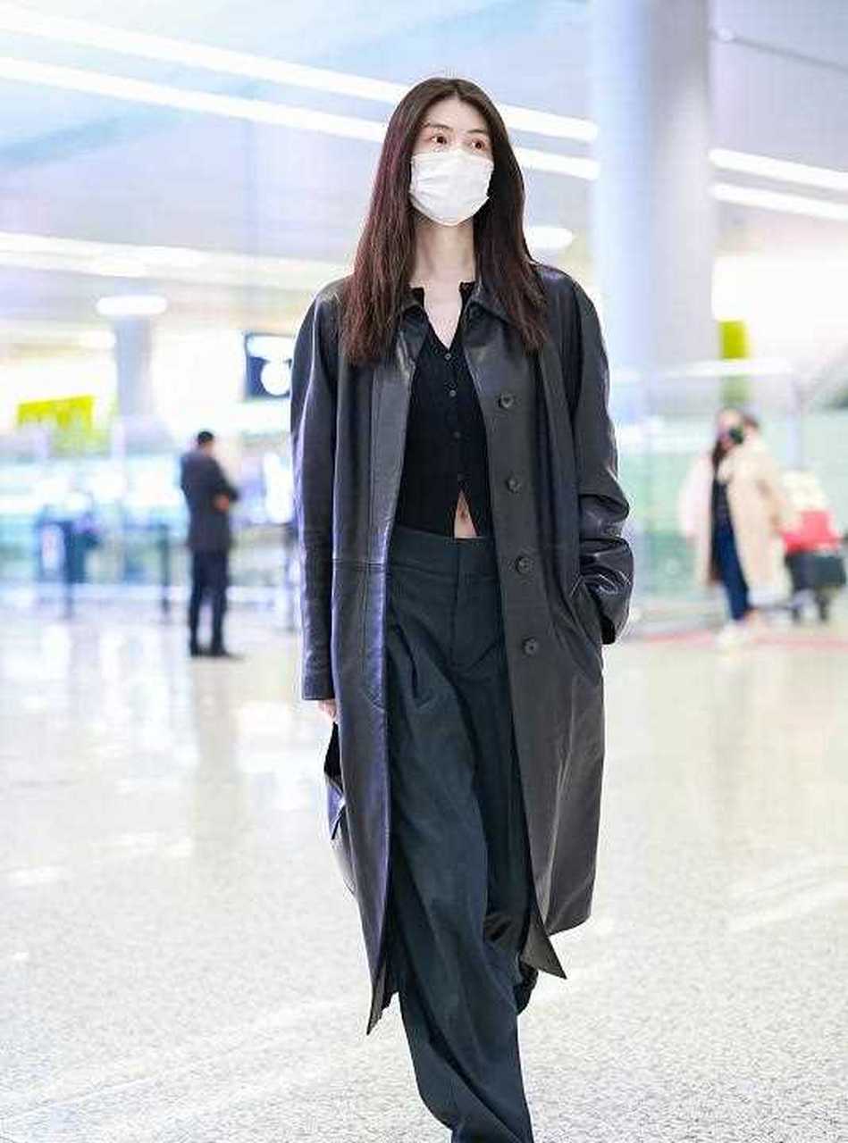 超模何穗街拍,她穿了一件黑色的长款皮风衣,内搭一件黑色的短款针织小